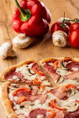 Top view of delicious Capricciosa Pizza on wooden table. Ingredients peeled tomato, cheese, ham, mushrooms, salami.