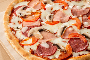 Top view of delicious Capricciosa Pizza on wooden table. Ingredients peeled tomato, cheese, ham, mushrooms, salami.