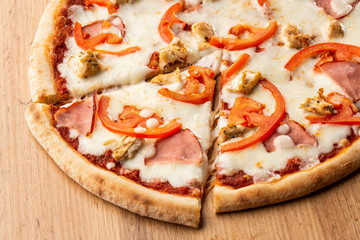 Flat lay with traditional Italian pizza with chicken, ham, cheese and tomatoes on wooden  back.