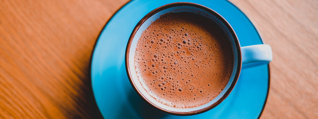Brown cacao in bright blue mug on a wooden table.