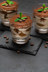 Classic tiramisu dessert in a glass on stone serving board on dark concrete background