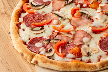 Top view of delicious Capricciosa Pizza on wooden table. Ingredients peeled tomato, cheese, ham, mushrooms, salami.