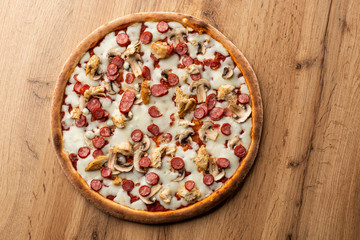 Tasty Italian pizza on wooden  background. Top view of pizza with sausages, chicken, mushrooms, tomatoes and cheese. 