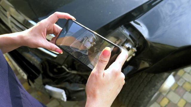 a woman takes a photo on her smartphone after the crash of a broken car bumper