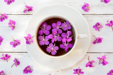 Fototapeta na wymiar White cup with a tea from the flowers of fireweed on white wooden background top view
