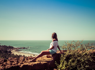 Girl sitting on the wall of the fort on the background of the beach Vagator