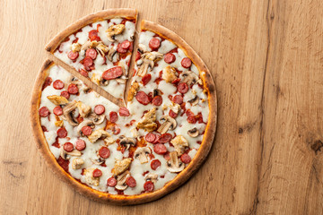 Tasty Italian pizza on wooden  background. Top view of pizza with sausages, chicken, mushrooms, tomatoes and cheese. 
