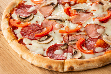 Top view of delicious Capricciosa Pizza on wooden table. Ingredients peeled tomato, cheese, ham, mushrooms, salami.