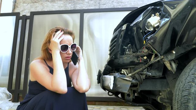 car accident concept. woman in a state of shock talking on the phone after a car accident, standing by a car with a broken bumper