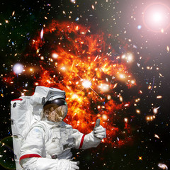 Astronaut gives thumbs-up against outer space, galaxies and stars. The elements of this image...