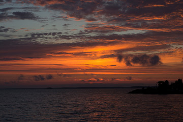 bright colorful sunset with pink orange yellow and gold overflows with dark clouds above water and  solar track on the water, big lake in Rissia