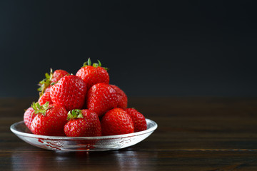 Freshly picked organic strawberries in a glass bowl. Dark wooden table, water, high resolution