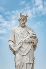 Fototapeta premium Statue of priest with figure of crucified Jesus in Vienna downtown at blue sky background, Austria