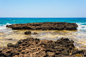  black and yellow rocks and stones and blue sea on the shore of Ayia Napa, Cyprus