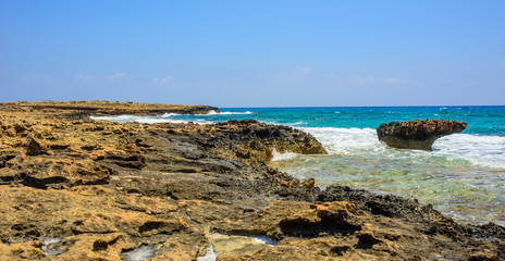 Fototapeta na wymiar black and yellow rocks and stones and blue sea on the shore of Ayia Napa, Cyprus