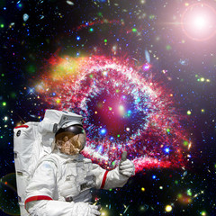 Astronaut gives thumbs-up against outer space, galaxies and stars. The elements of this image...