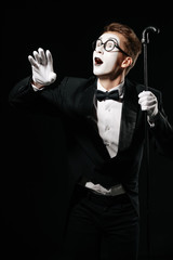 surprised mime man in tuxedo and glasses posing with walking stick on black background
