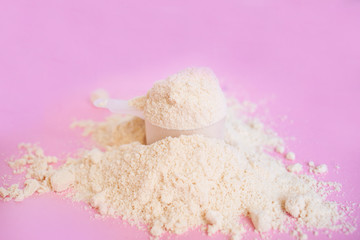 heap of whey protein powder with plastic spoon on pink background closeup