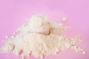 heap of whey protein powder with plastic spoon on a light pink background