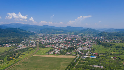 Fototapeta na wymiar Aerial view of the Svalyava in Carpathian mountains. Natural background with geometric pattern - beige and red rectangles of the fields and roofs and lines of roads and trees. Zakarpattia, Ukraine.