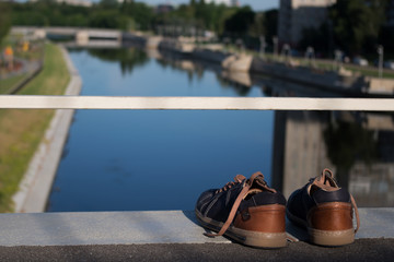 A pair of woman’s sneakers standing against a white railing on the edge of the bridge over the...