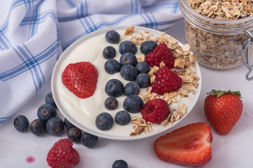 White yogurt in bowl with oatmeal and strawberries, blueberries and raspberries on the top on white...