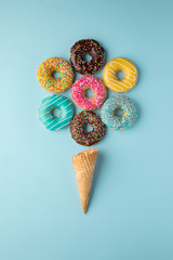 Colorful donuts in ice-cream shape with waffle cone on light blue background. 