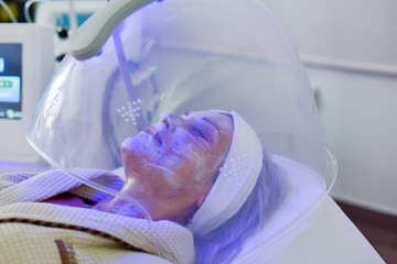 Woman receiving color light therapy for face. Facial therapy. Anti-aging procedures.