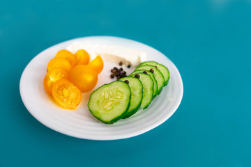Greek salad, yellow tomato, cucumber, white cheese, black pepper on the white plate on the blue background