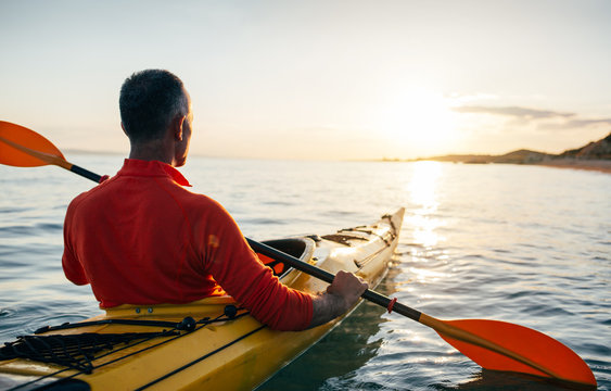 Rear view of older man enjoy kayaking on the sunset sea