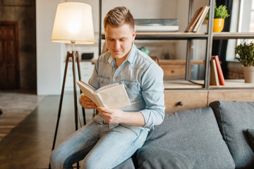 Young man sitting in couch and reading a book