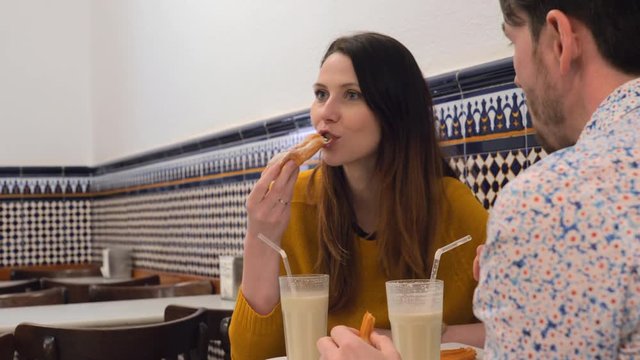 Young man and woman eating in Valencian cafe and enjoying horchata with fartons and churros. Refreshing tigernut drink