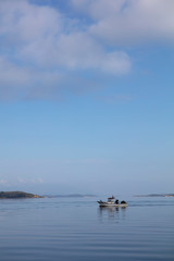 Colorful Fishing Boat Sailing on Sea with Reflections Over Blue Cloudy Sky at Morning Time