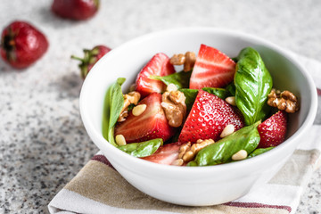 Fresh spinach salad with strawberries and nuts on a gray background. Summer salad with strawberries