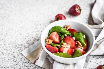 Fresh spinach salad with strawberries and nuts on a gray background. Summer salad with strawberries