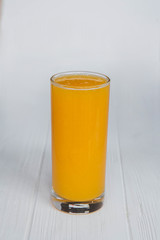 A thin, high transparent glass is filled with freshly prepared citrus juice which stands on an isolated wooden background of white color.