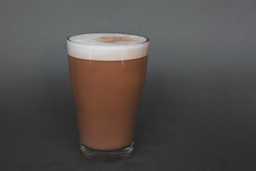 A large transparent glass filled with cold summer drink with milk and green tea powder is photographed on a gray, isolated background, photo for the menu