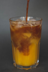 A large transparent glass filled with cold summer drink Latte with orange juice cooked in a coffee shop of the third wave. gray, isolated background, photo for the menu