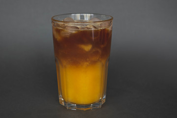 Fototapeta na wymiar A large transparent glass filled with cold summer drink Latte with orange juice cooked in a coffee shop of the third wave. gray, isolated background, photo for the menu