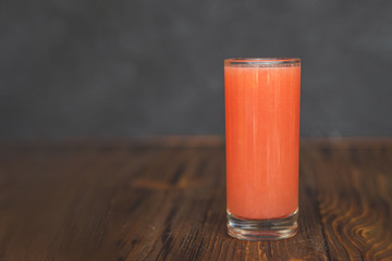 A thin, high transparent glass is filled with freshly prepared citrus juice which stands on an wooden table and grey background.