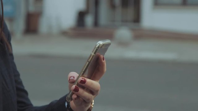 [Slow motion] Close-up of girl swiping on mobile phone in her hand. Young woman holding smartphone on the street. Close view of mobile phone in person's hand.