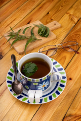 Tasty nettle tea in a cup. Freshly cut nettle and infected tea on a wooden table.