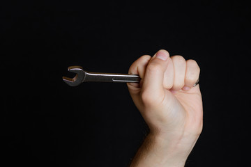 Wrench holds men's hand isolated on black background close-up
