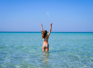 Slim and athletic girl in a colourful bikini having fun on a wonderful beach with crystal clear water -vacation-fitness-wellness