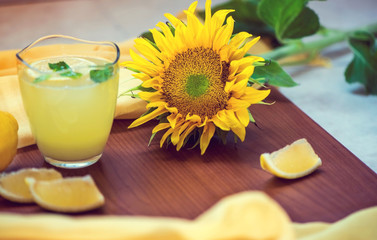 Mint lemonade with lemon slices on a wooden background with a beautiful sunflower, still life photography, close up