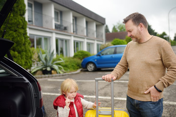 Handsome man and his little son going to vacations, loading their suitcase in car trunk. Automobile trip in the countryside. Roadtrip for family with kids