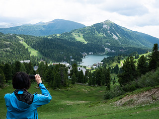 Woman is taking a picture with her mobile phone from a mountain lake