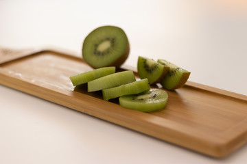 A beautifully sliced kiwi lies on a wooden board against a white background