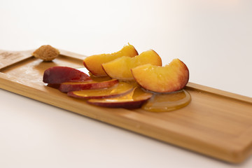 A beautifully sliced peach poured with honey is lying on a wooden board on a white background