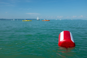 Lake Balaton summer with sailboats, kayakers and a red buoy in the foreground